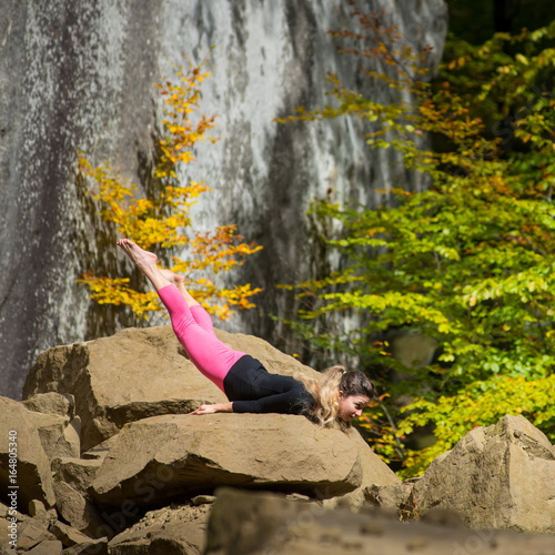 Sporty fexible woman is practicing yoga on the boulder in the nature. Huge rocks on the background photo