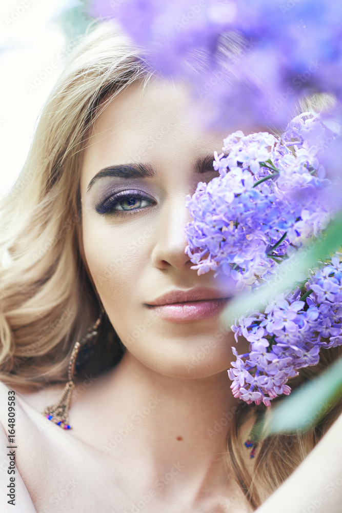 Outdoor fashion beautiful young woman surrounded by lilac flowers summer. Spring blossom lilac bush. Portrait of a girl blondes Outdoor fashion beautiful young woman surrounded by lilac flowers summer. Spring blossom lilac bush. Portrait of a girl blondes