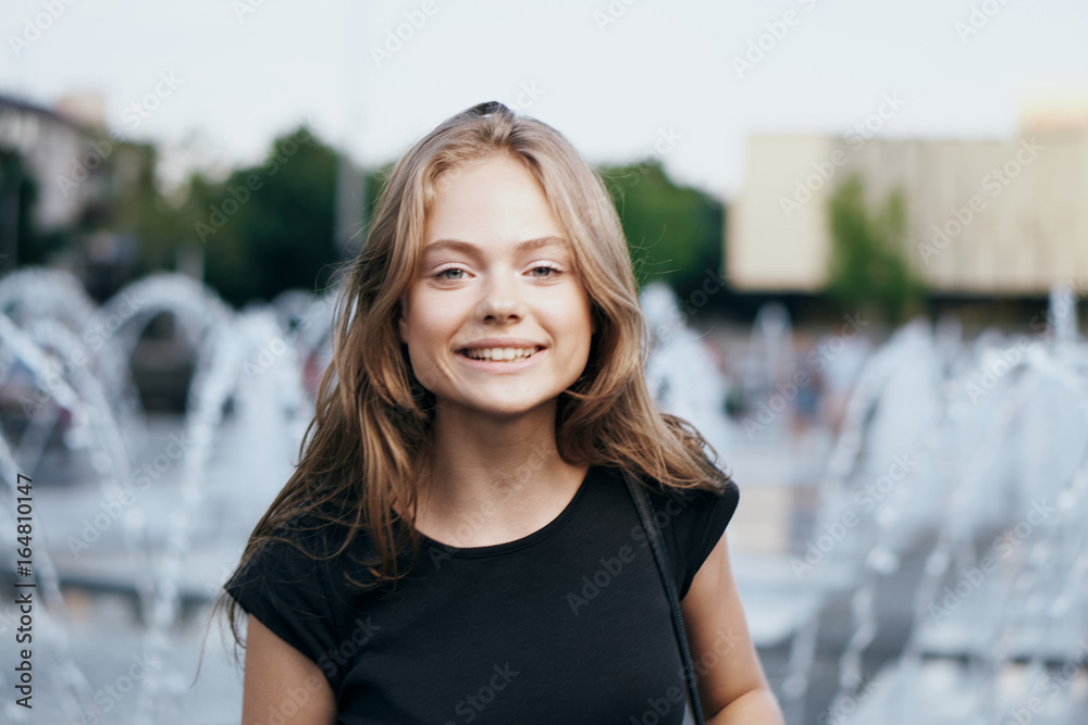 Young beautiful woman is walking in the park on the street near the fountain Young beautiful woman is walking in the park on the street near the fountain