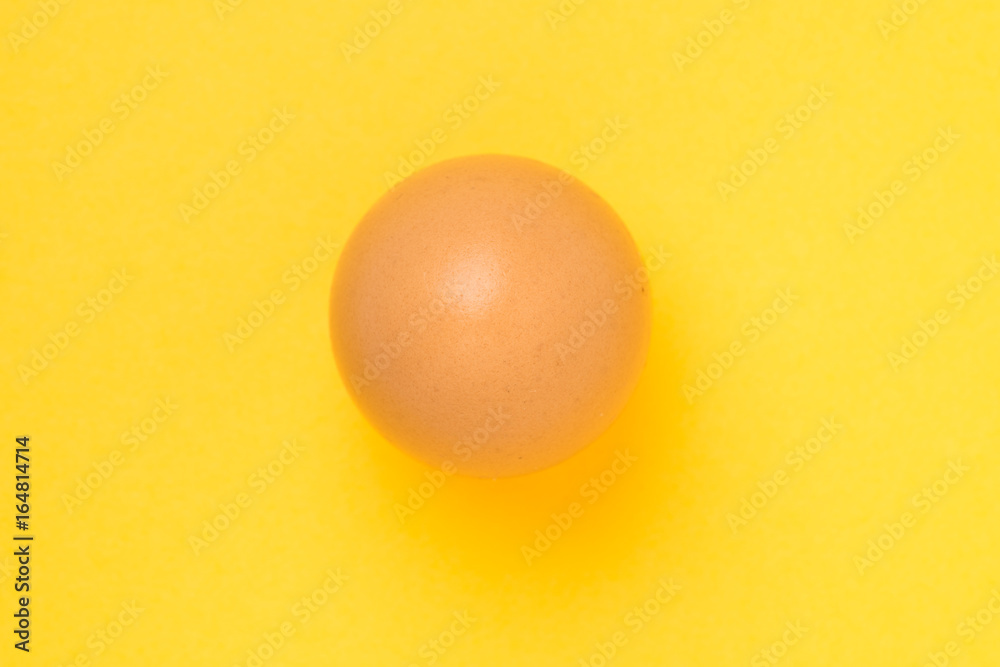 Single brown chicken egg on yellow background Single brown chicken egg on yellow background