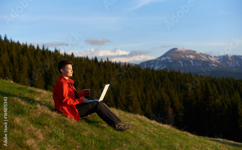 Shot of a cheerful young female working on her laptop resting on top of the mountain on sunset after hiking copyspace nature achievement project education travelling.