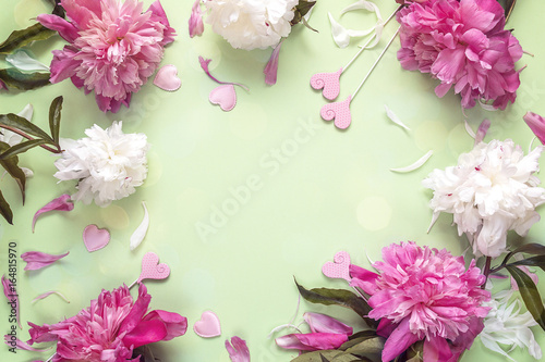 Fototapeta Naklejka Na Ścianę i Meble -  Frame of peonies and decorative hearts on green background. Place for the text.