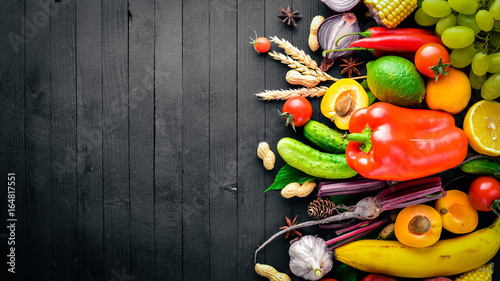 Large selection of raw vegetables and fruits on a black wooden table. Free space for your text. Top view.