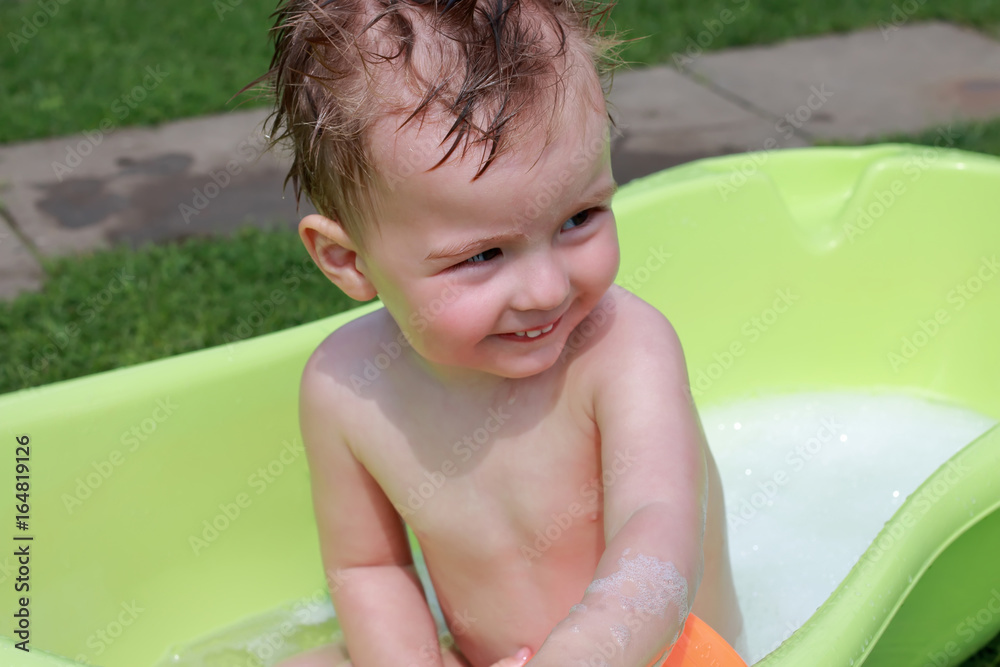 Happy baby boy taking water procedures in summer garden Happy baby boy taking water procedures in summer garden