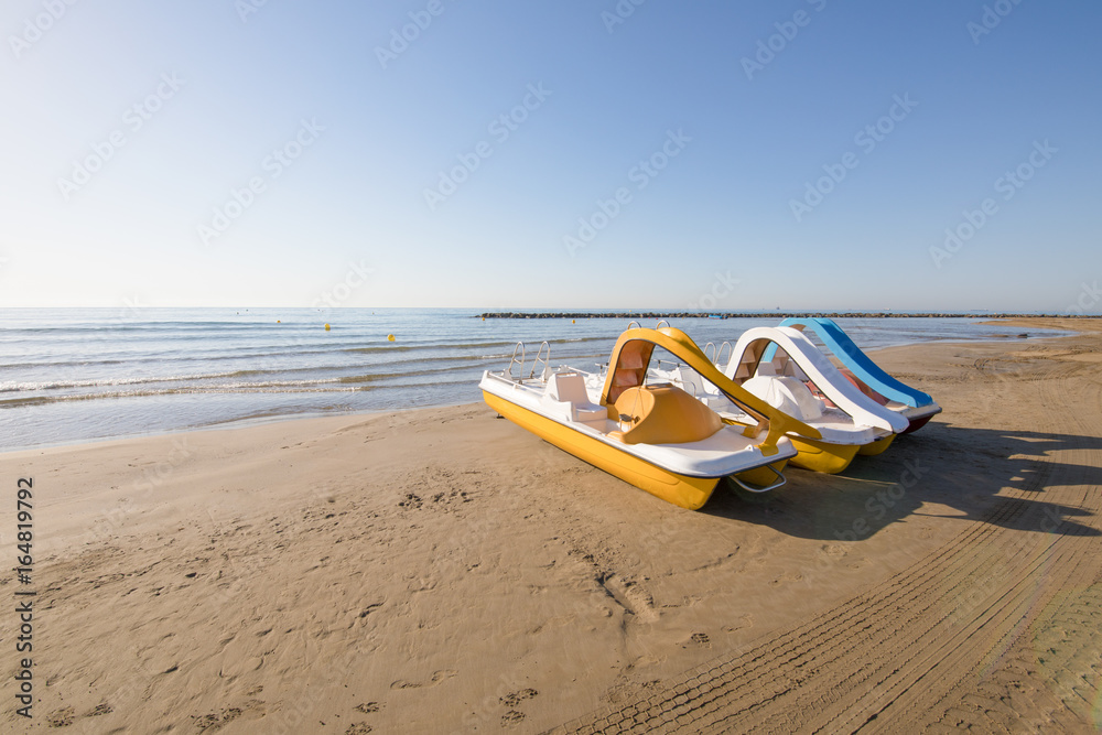 three pedal boats in row on the beach Els Terrers, in Benicassim,  Castellon, Valencia, Spain, Europe. Blue clear sky and Mediterranean Sea  Stock Photo | Adobe Stock