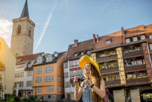 Young woman tourist in yellow hat standing with photo camera on the famous Merchants bridge background in Erfurt city, Germany photo