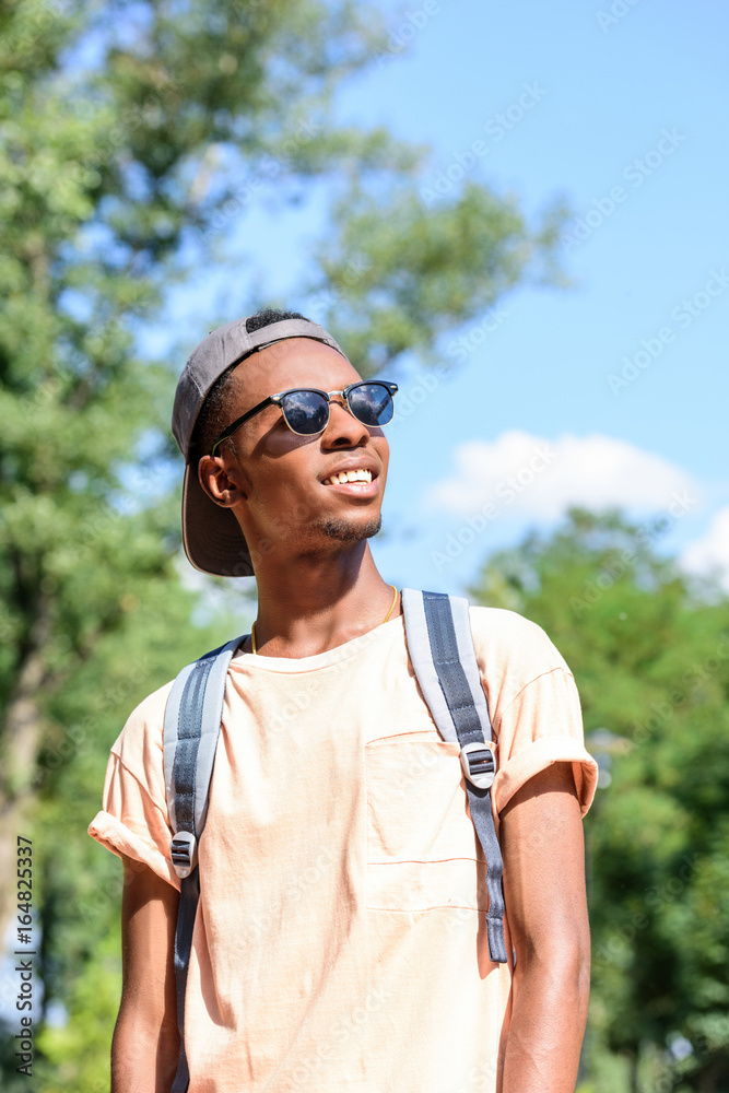 portrait of smiling african american man in sunglasses and cap looking away