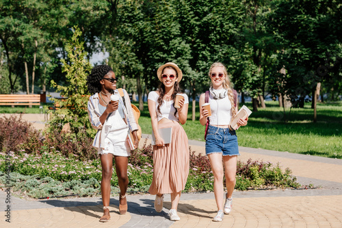 happy multicultural women with disposable cups of coffee in hands walking in park © LIGHTFIELD STUDIOS