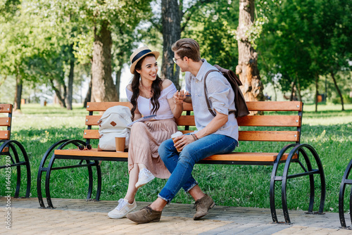 happy multicultural couple having conversation while sitting on bench