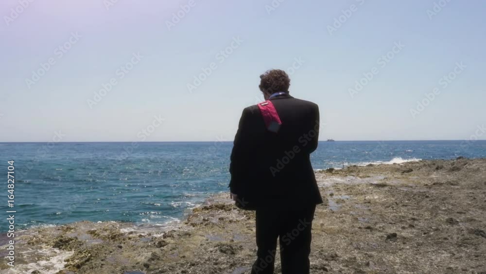 Man in suit talking on his smartphone on a deserted island in front of the ocean Man in suit talking on his smartphone on a deserted island in front of the ocean