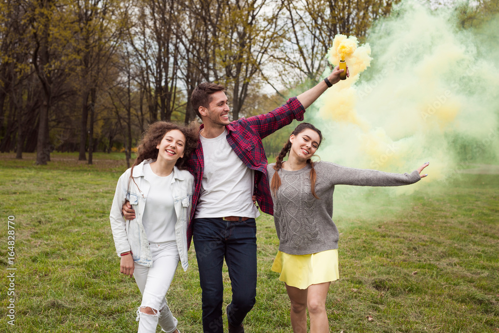 Obraz premium Youngsters walking with colored smoke in park