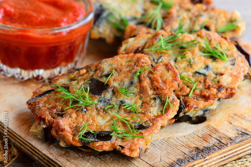 Quick and easy eggplant cutlets. Fried eggplant cutlets with garlic and dill on a wooden board. Tomato sauce in a glass bowl. Healthy veggie recipe. Closeup