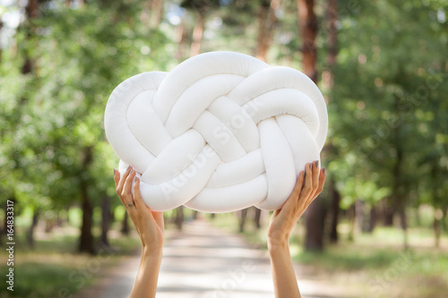 Hands hold white knot pillow in forest, can be used for Background for different art