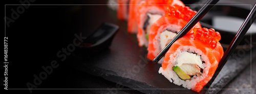 Japanese cuisine.Sushi roll with salmon eel and red caviar. One peace in chopsticks.