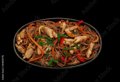 Soba noodles with chicken meat on a stone plate over dark background