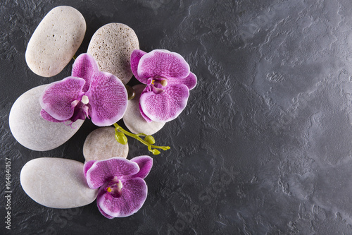 Lilac orchids and white stones lie on black marble. Spa.
