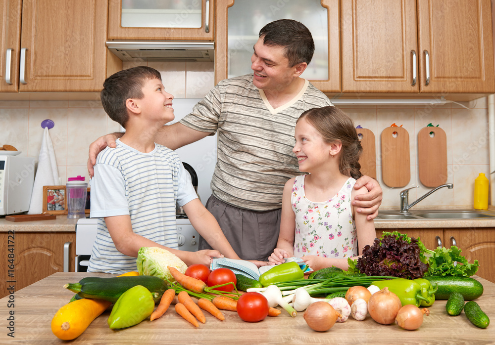 Father and two children reading cooking book and choice dishes. Happy family, girl and boy having fun with fruits and vegetables in home kitchen interior. Healthy food concept. Father and two children reading cooking book and choice dishes. Happy family, girl and boy having fun with fruits and vegetables in home kitchen interior. Healthy food concept.