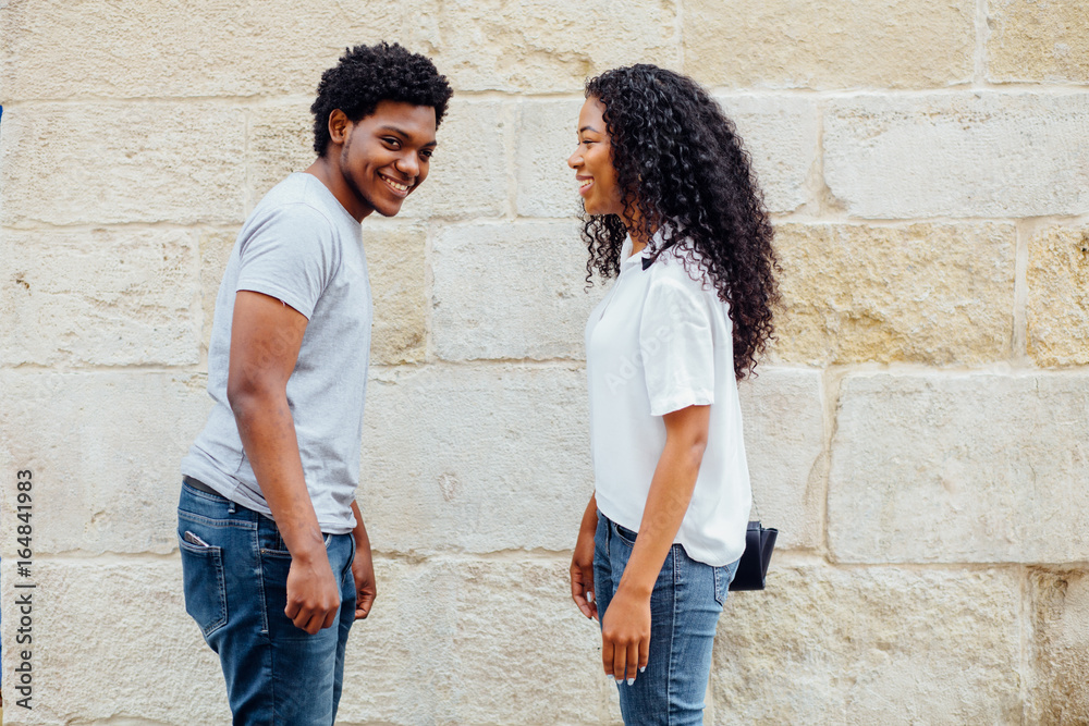 Happy Young Dark Skin Couple Facing Each Other on a Light Wall Background, Emphasizing Copy Space.