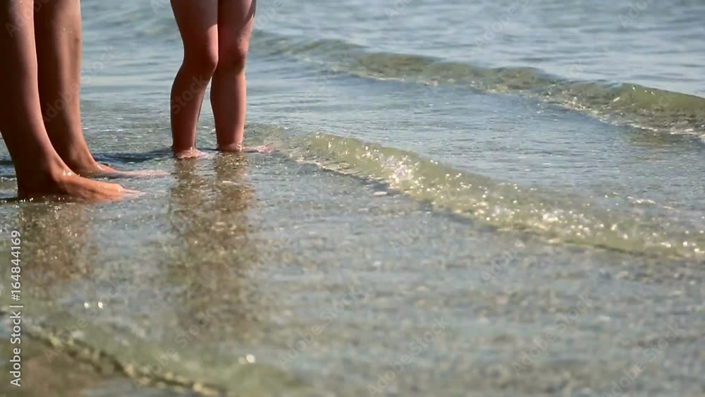 Mom's feet with baby in the sea. Wave washes children's legs Mom's feet with baby in the sea. Wave washes children's legs