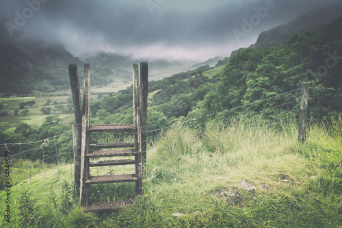 Wooden Ladder Over Fence Crossing with Spectacular View over Misty Valley in Snowdonia National Park
