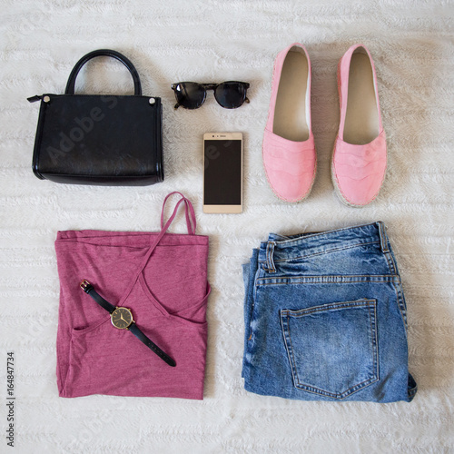 perfect summer outfit accessories. flat lay of a trendy woman fashion outfit. denim jeans, pink top shirt, espadrilles, sunglasses, black purse and a elegant smartphone. top view.