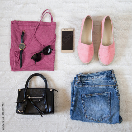 perfect summer outfit accessories. flat lay of a trendy woman fashion outfit. denim jeans, pink top shirt, espadrilles, sunglasses, black purse and a elegant smartphone. top view.