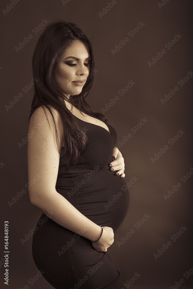 Studio shot of a beautiful pregnant woman holding hands on her big belly Studio shot of a beautiful pregnant woman holding hands on her big belly