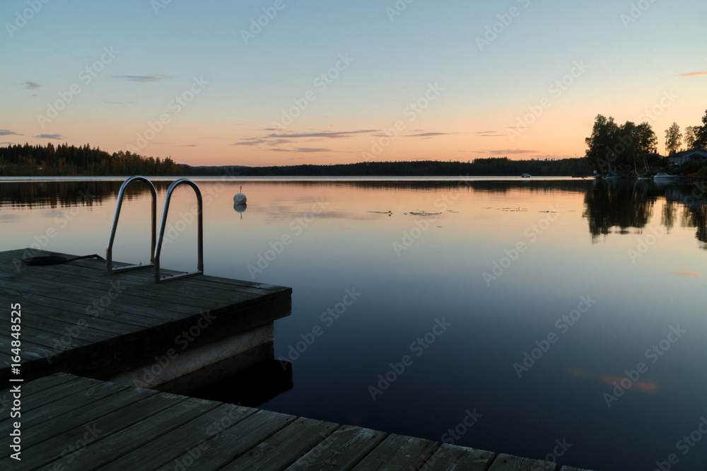 Calm summer evening sunset, jetty with ladder in reflection lake