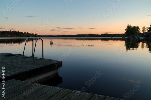 Calm summer evening sunset, jetty with ladder in reflection lake