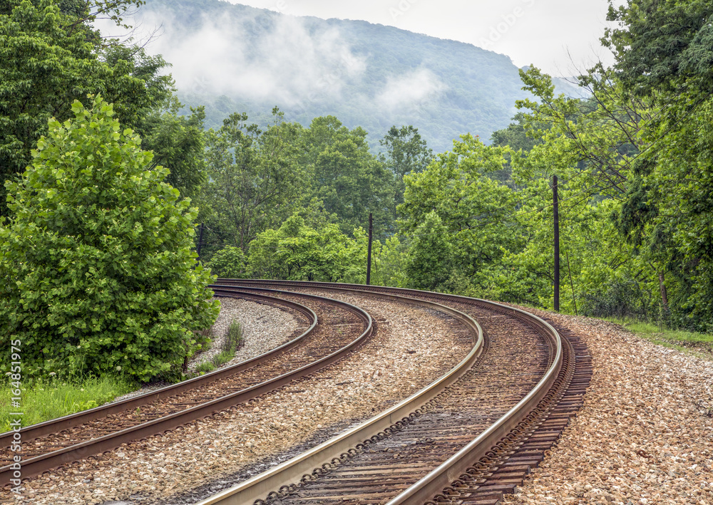 Naklejka premium Curving Double Railroad Tracks through Foggy Mountains