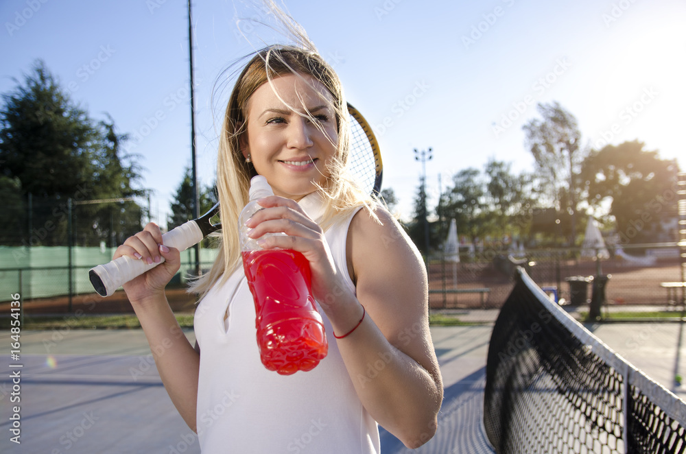 young female tennis player drinking energy drink, water with