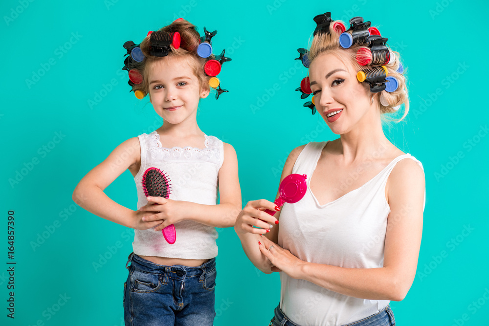Mother and little daughter in hair curlers on a turquoise background in the studio Mother and little daughter in hair curlers on a turquoise background in the studio