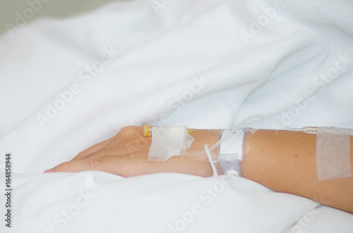 Patient being treated by saline solution via arm. Hand and arm with saline solution tube on hospital bed.