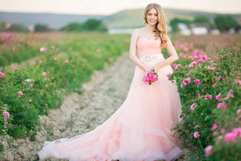 Beautiful pretty woman with long curly hair posing near pink roses in a garden Beautiful pretty woman with long curly hair posing near pink roses in a garden