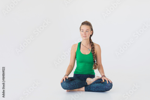 Young attractive woman practicing yoga. Close up portrait of attractive woman sitting in meditating position on white floor. Young girl raising hands doing yoga.