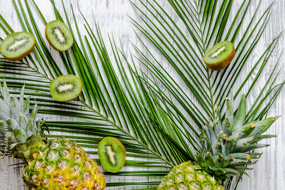 Fototapeta Summer exotic fruits. Kiwi, pineapple and palm branch on wooden background top view