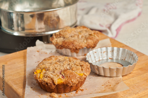 Fresh, baked peach streusel coffee cake and tin mold, cooling on parchment paper on a wood cutting board and napkin