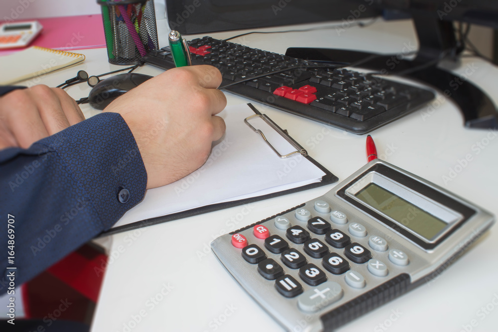 man writing notes from computer on wooden table. Man hand with pen, calculator and computer on wooden table