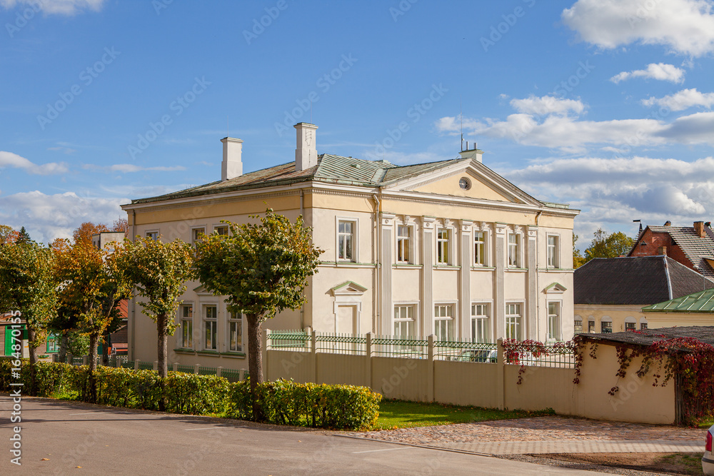 Pretty town view with shaped trees and bushes and yellow stone building. Historical center of Eastern Latvia - Aluksne.