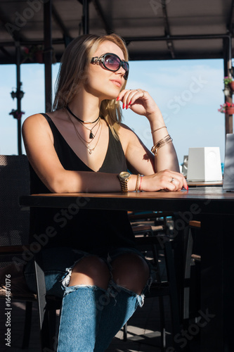 Beautiful blond girl sits at a table in a cafe on the street photo