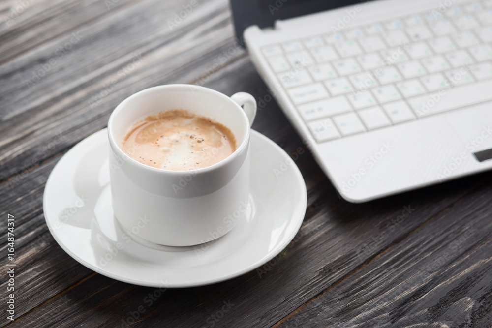 Coffee cup close up and laptop as background on wooden table Coffee cup close up and laptop as background on wooden table