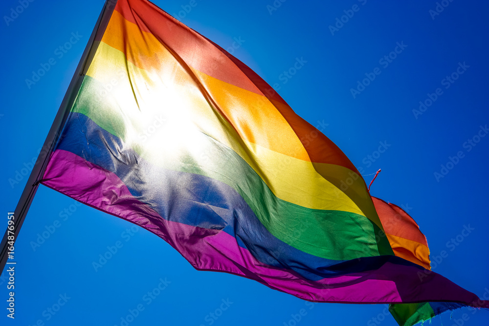 Rainbow flag waiving in the wind with sun shining through it