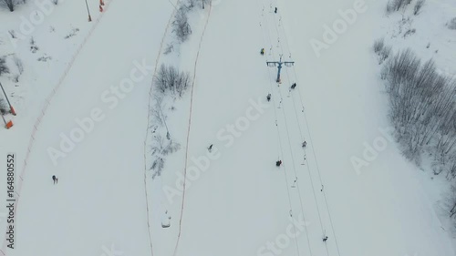 Aerial view: Skiers and snowboarders going down the slope in winter day. Skiers and snowboarders enjoying on slopes of ski resort in winter season. 4K video, aerial footage.