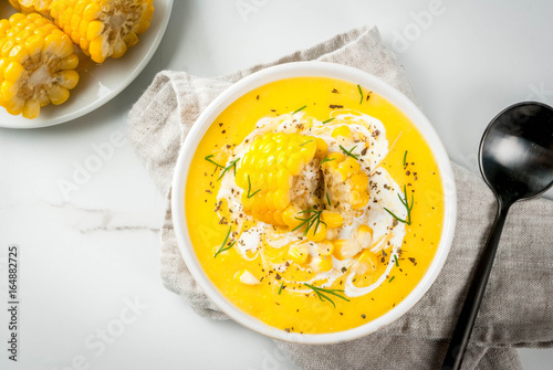 Vegan cuisine. Traditional autumn corn soup. Served with corn cobs, greens, cream. On a white marble table. Copy space top view