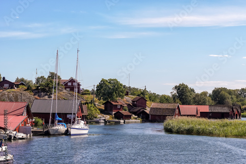 A small harbor with some boathouses and some red cottages in background on the swedish island Harstena in the archipelago of Gryt in the Baltic Sea.