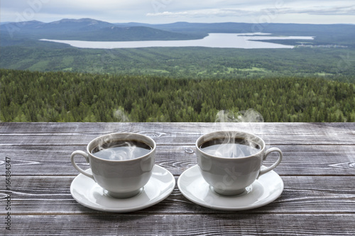 Two cups of fresh hot coffee for a pair of lovers against the backdrop of mountains, lakes, forest. Nature.