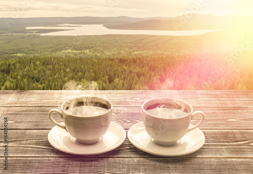Two cups of fresh hot coffee for a pair of lovers against the backdrop of mountains, lakes, forest. Nature. Against the background of dawn.