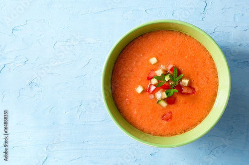 Summer cold soup gazpacho with parsley and vegetables on blue concrete background.