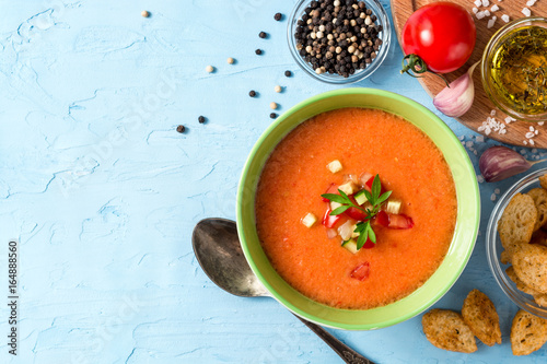 Summer cold soup gazpacho with parsley and vegetables on blue concrete background.