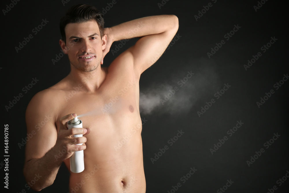 Handsome young man with deodorant on dark background